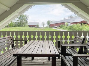 A covered outdoor seating area with benches and a table, overlooking a grassy field and buildings. - 5 Person Holiday Home in Kristdala (Kristdala)