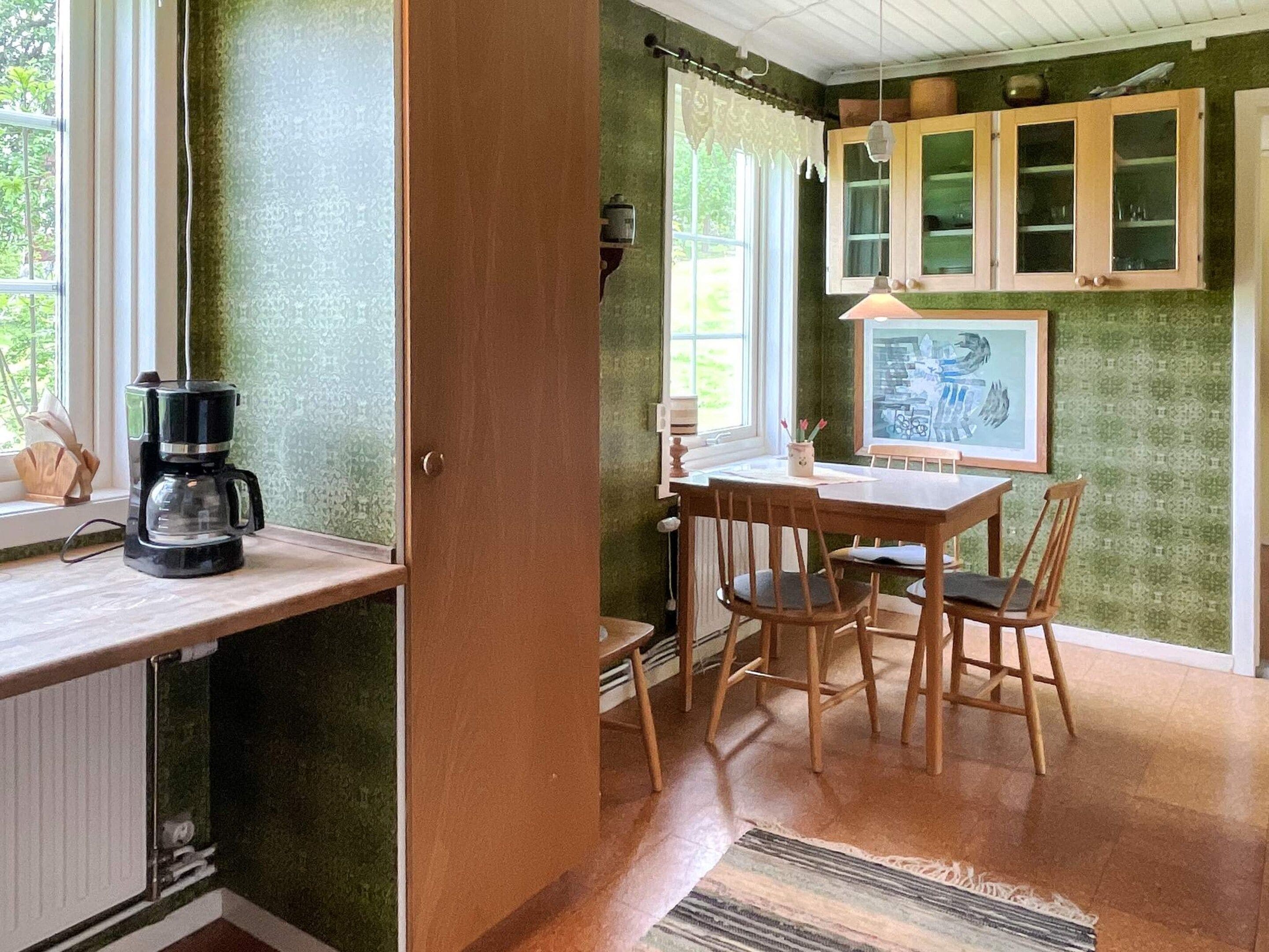Una habitación con una mesa de madera, sillas, una cafetera y un ventanal con cortinas.