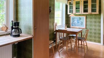 Una habitación con una mesa de madera, sillas, una cafetera y un ventanal con cortinas.