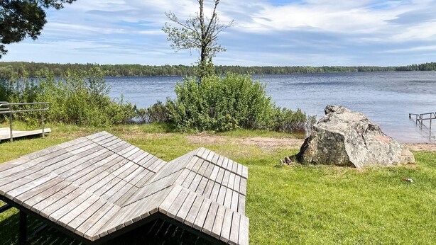 Ein Holzdeck mit Metallgeländer, ein großer Felsen und ein Baum in einer Uferlage.