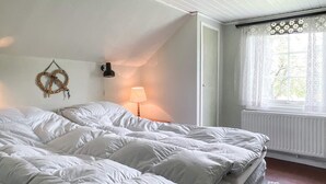 Ein Schlafzimmer mit einem großen Bett, einer Wandlampe, einem Fenster mit Vorhängen und einer Heizung.
