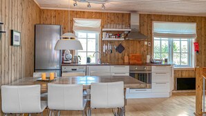 Una cocina con paredes de madera, una isla central con sillas, un refrigerador, estufa y una ventana con persianas.