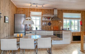 Eine Küche mit Holzwänden, einer zentralen Kochinsel mit Stühlen, einem Kühlschrank, einem Herd und einem Fenster mit Jalousien.