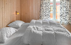 Ein Zimmer mit einer Holzwand, einem Bett mit weißer Bettwäsche und einem Fenster mit gemusterten Vorhängen.