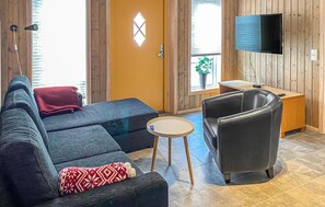 Ein Zimmer mit einer Couch, einem Sessel, einem kleinen Tisch, einem an der Wand befestigten Fernseher und einer Tür mit Fenster.