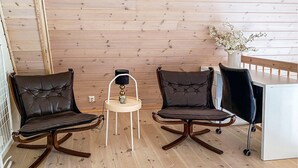 A room with wooden panel walls, two leather chairs with wooden frames, a small table with a lamp, and a white cabinet.