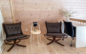 Une pièce aux murs recouverts de lambris en bois, deux fauteuils en cuir à ossature en bois, une petite table avec une lampe et un meuble blanc.