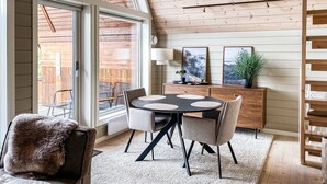 A dining area with a round table, chairs, and a view through large windows.
