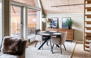 Un espace repas avec une table ronde, des chaises et une vue dégagée grâce à de grandes fenêtres.