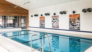 An indoor swimming pool with clear water, a metal ladder, and a tiled floor.