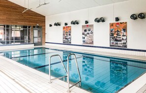 Une piscine intérieure à l’eau claire, avec un escalier en métal et un sol carrelé.