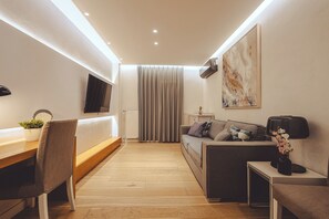 Ein modernes Wohnzimmer mit einer Couch, einem Esstisch, einem Sessel, einem Fernseher und einem Bild an der Wand.