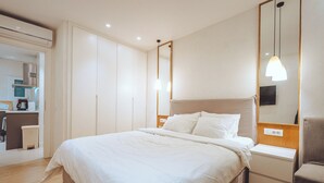 Hotellihuone, jossa on sänky, yöpöytä, pieni sivupöytä ja peili.