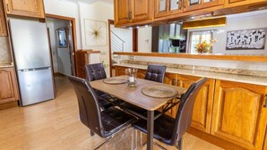 A kitchen with wooden cabinets, a stainless steel refrigerator, a dining table with chairs, and a kitchen island with a sink. - Villa Mariela by NPMallorca (Sa Coma)