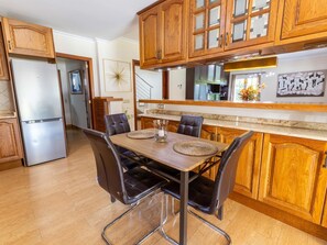 A kitchen with wooden cabinets, a stainless steel refrigerator, a dining table with chairs, and a kitchen island with a sink. - Villa Mariela by NPMallorca (Sa Coma)