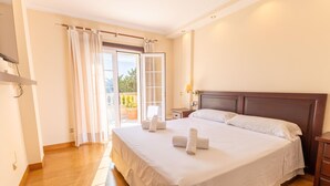 A hotel room with a large bed, a bedside table, a nightstand, a window with curtains, and a view of the outdoors. - Villa Mariela by NPMallorca (Sa Coma)