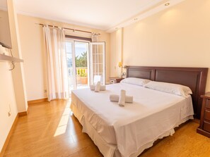 A hotel room with a large bed, a bedside table, a nightstand, a window with curtains, and a view of the outdoors. - Villa Mariela by NPMallorca (Sa Coma)