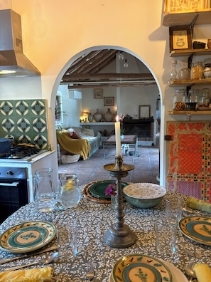 A dining area with a table set for two, a candle centerpiece, and a view into a living room through an archway.