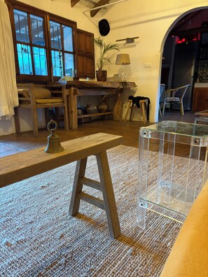 A rustic interior with a wooden table, a clear glass display case, a woven rug, and a plant.
