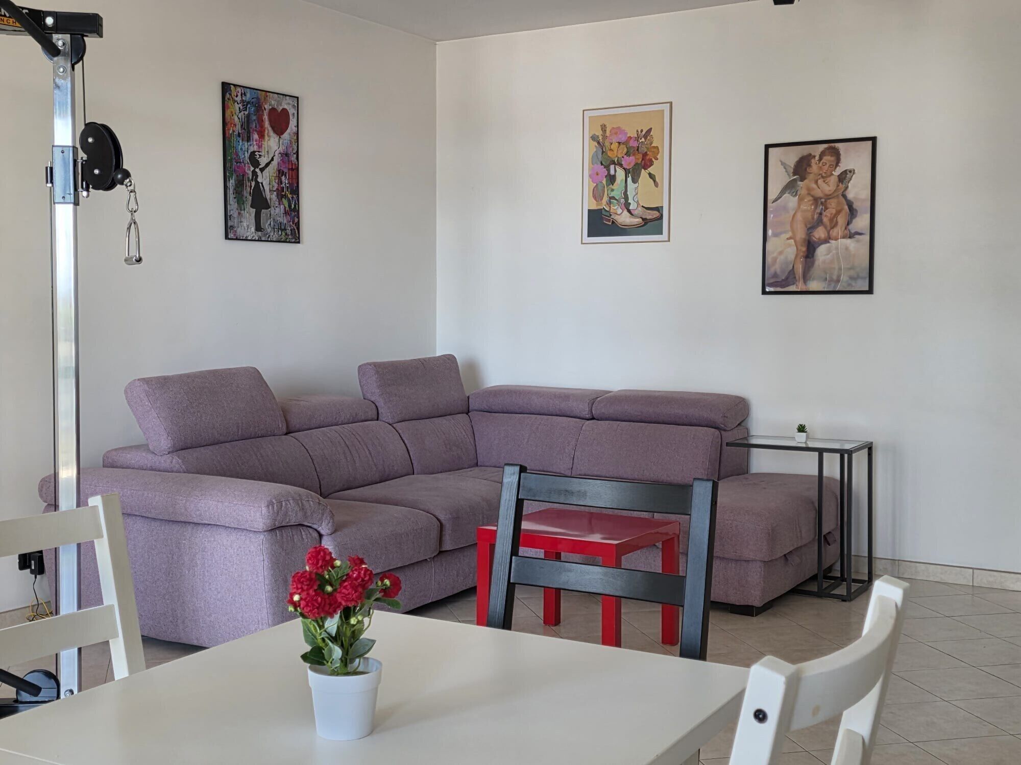 Una sala moderna con un sofá seccional, una pequeña mesa de comedor y una silla roja. Hay tres obras de arte enmarcadas en la pared.