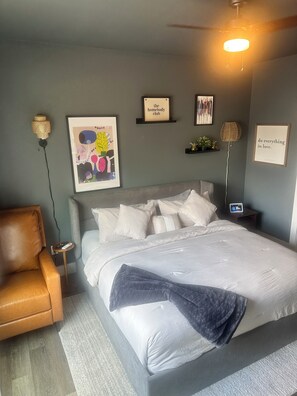 Ein Schlafzimmer mit Bett, Sessel, Nachttisch, Lampe und Wanddekorationen.
