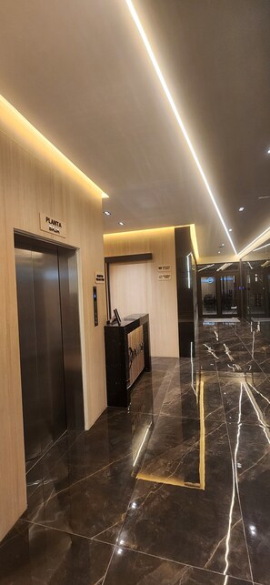 A modern hotel lobby with a reception desk, an elevator, and a sign indicating the direction to the plant room. - Premium loft hasta 4 huespedes zona UPAEP y Av. Juárez (Heroica Puebla de Zaragoza)