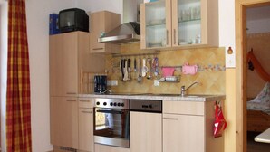 Una cocina compacta con estufa, horno y lavavajillas, armarios de madera y un pequeño televisor.