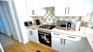 Una cocina compacta con armarios blancos, microondas, tostadora y estufa a gas.