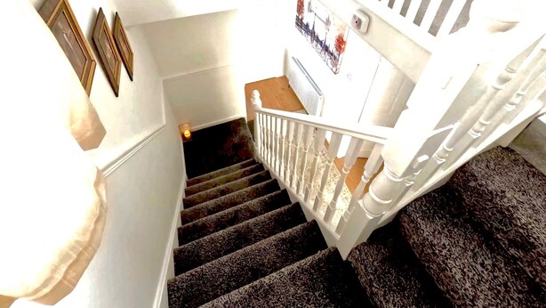 Una escalera con barandilla blanca, un cuadro en la pared y una lámpara.