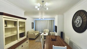 Un comedor con mesa y sillas de madera, un armario blanco con puertas de cristal, un sofá y un reloj de pared grande.