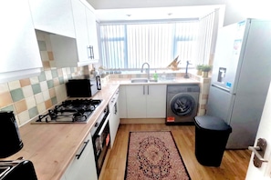 A compact kitchen with a gas stove, a washing machine, and a refrigerator.