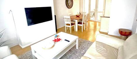 Een woonkamer met een witte bank, een witte salontafel en een eetgedeelte met een houten tafel en witte stoelen.