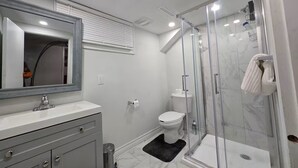 Ein modernes Badezimmer mit einer gläsernen Duschkabine, einem weißen Waschbecken und einem großen Spiegel.