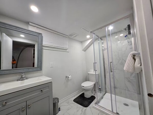 Ein modernes Badezimmer mit einer gläsernen Duschkabine, einem weißen Waschbecken und einem großen Spiegel.