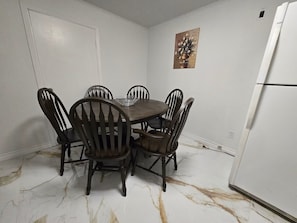 A dining area with a marble floor, a white refrigerator, and a painting on the wall.
