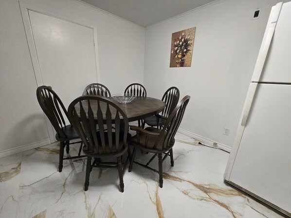 A dining area with a marble floor, a white refrigerator, and a painting on the wall.