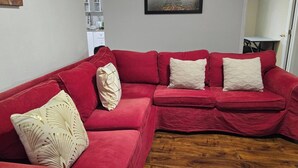 Ein rotes Ecksofa mit gemusterten Kissen, ein gerahmtes Landschaftsbild und ein Holzboden.