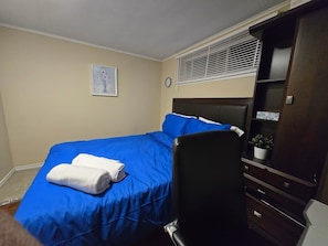 A bedroom with a bed, a chair, a dresser, a clock, and a window with blinds.
