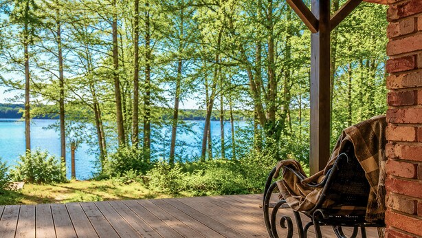 A wooden deck with a bench, overlooking a lake with trees and a clear sky.