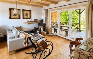 A cozy living room with a sofa, a rocking chair, a dining table, and a patio area with a wooden deck and a table.