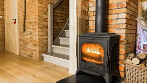 A wood-burning stove in a room with brick walls and a wooden staircase.