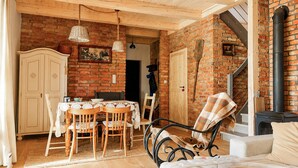A rustic room with a brick wall, wooden ceiling, a dining table with chairs, a sofa, and a fireplace.