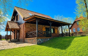 A rustic building with a sloped roof, a stone foundation, and a wooden porch.