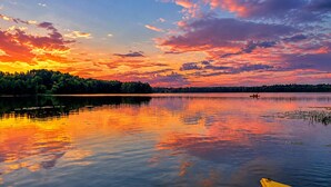 A calm lake at sunset with a forested shoreline and a small boat in the distance.