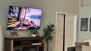 Ein Wohnzimmer mit Fernseher, Kamin, Topfpflanzen und einer Tür.