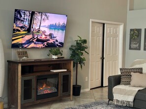 Ein Wohnzimmer mit Fernseher, Kamin, Topfpflanzen und einer Tür.