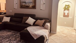 Ein Wohnzimmer mit einem dunkelgrauen Sofa, einem gemusterten Teppich und einem gerahmten Landschaftsbild an der Wand.
