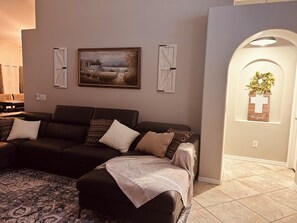 Ein Wohnzimmer mit einem dunkelgrauen Sofa, einem gemusterten Teppich und einem gerahmten Landschaftsbild an der Wand.