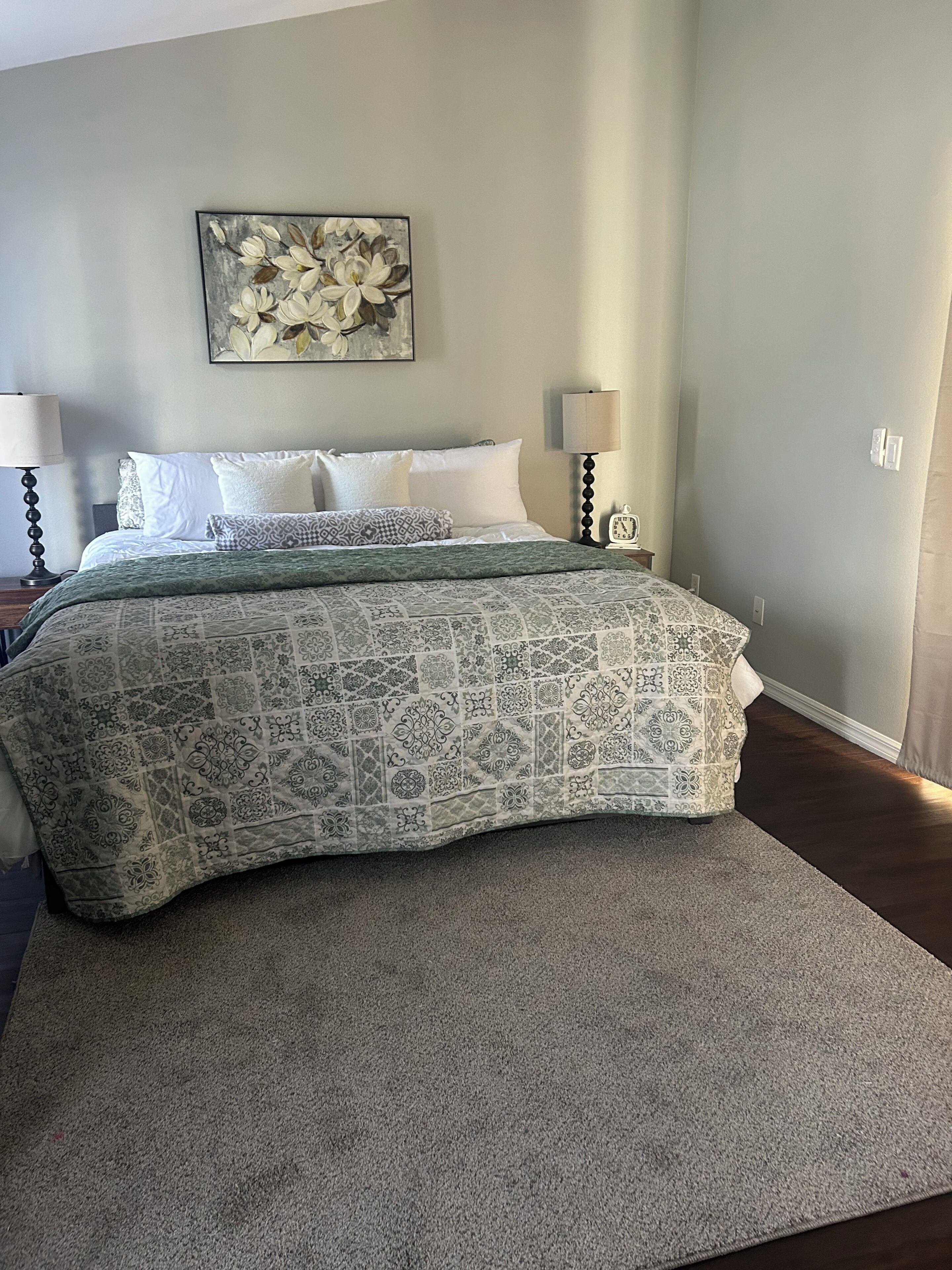 Une chambre à coucher avec un lit, des oreillers, une couverture, une horloge murale et un tableau.