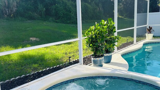 Ein Pool mit geschwungener Kante, umgeben von einem weißen Zaun, mit einem durch den Zaun sichtbaren Rasenbereich.